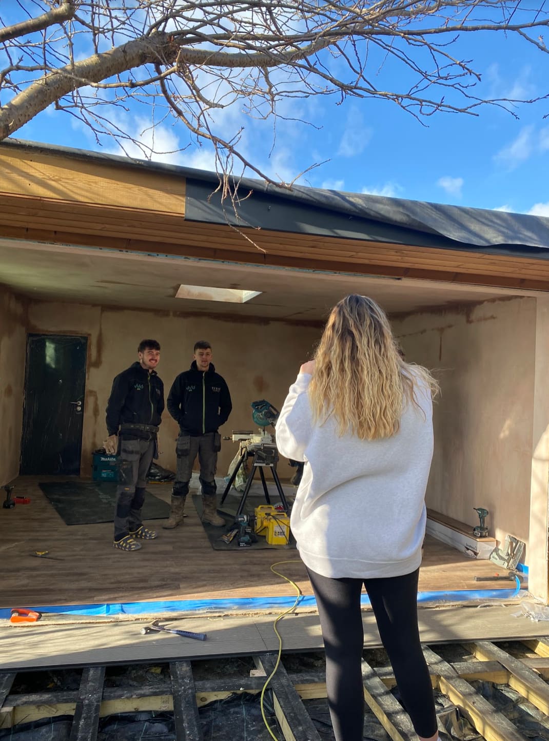Content creator filming two tradespeople on-site during a garden room build — behind the scenes trades content creation