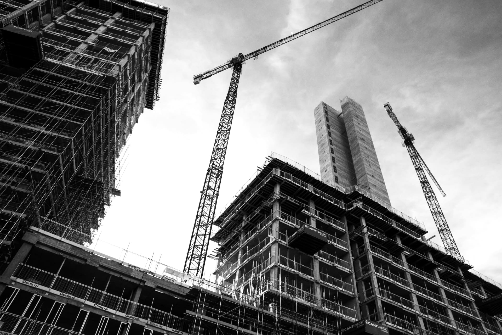 Black-and-white wide-angle view of a high-rise construction site with cranes and scaffolding — social media agency for construction businesses