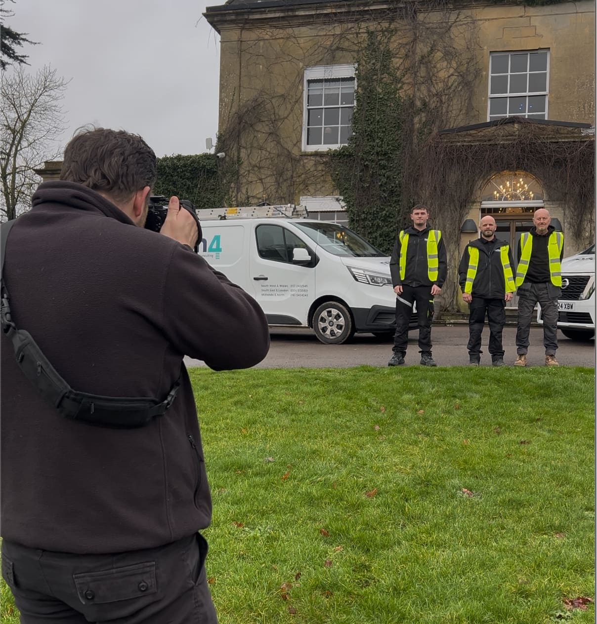 Compelite Pro photographer shooting a renovation team in branded hi-vis vests beside a company van outside a Georgian manor — behind the scenes renovation content