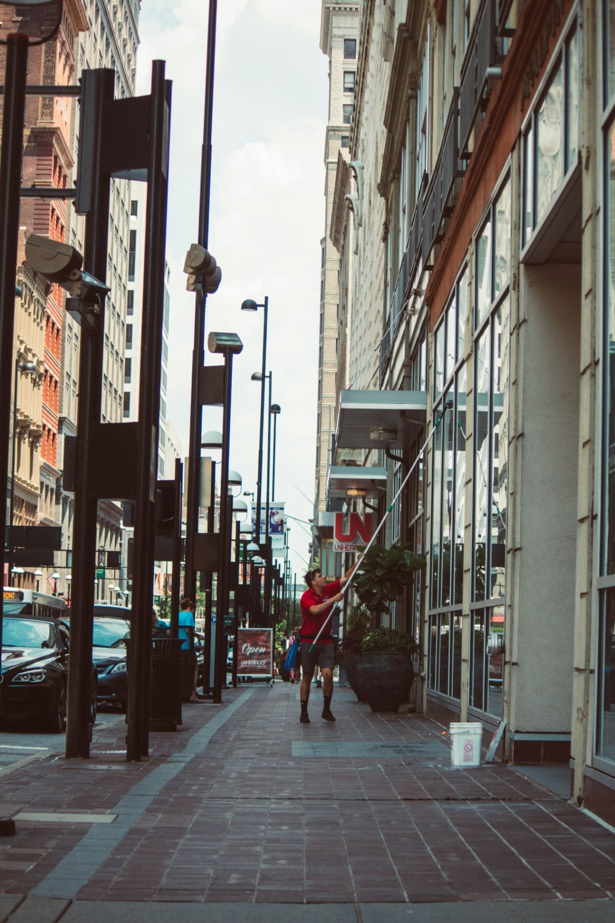 Window cleaner in a red shirt using an extendable water-fed pole to clean shop windows on a city high street — social media agency for window cleaning businesses